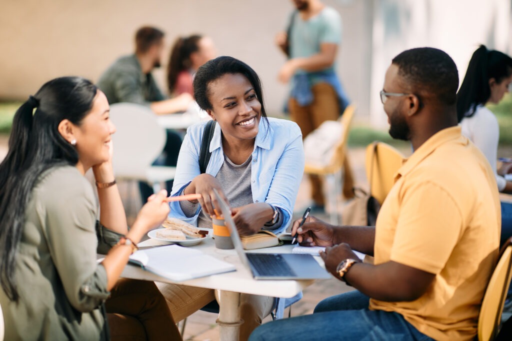 Happy black student and her college friends talking on lunch break at campus.