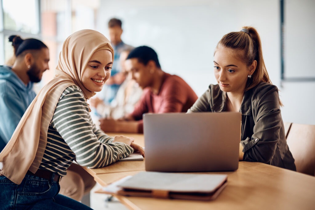 Happy female students using laptop during computer class at the university.