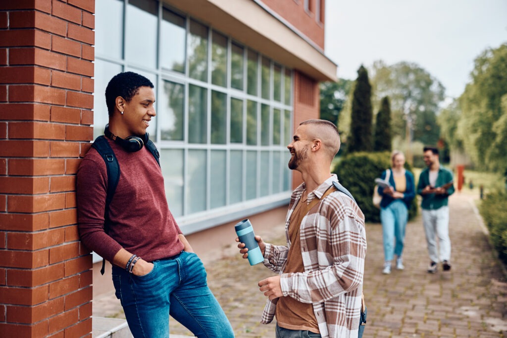 Happy male students talking in front of university building.