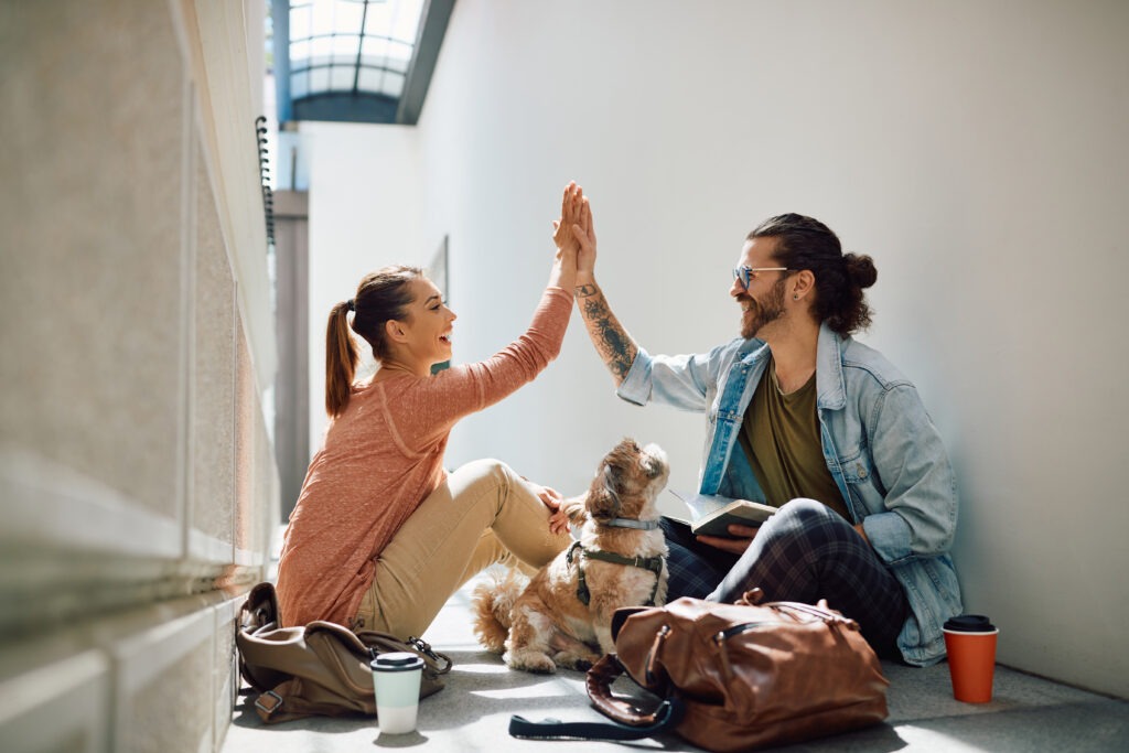 Happy university friends giving high-five while learning together in a hallway.