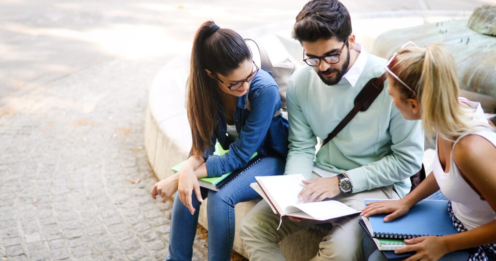 Happy young university students friends studying with books at university