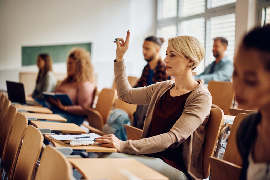 Mid adult student raising her hand to ask a question during a class at the university.