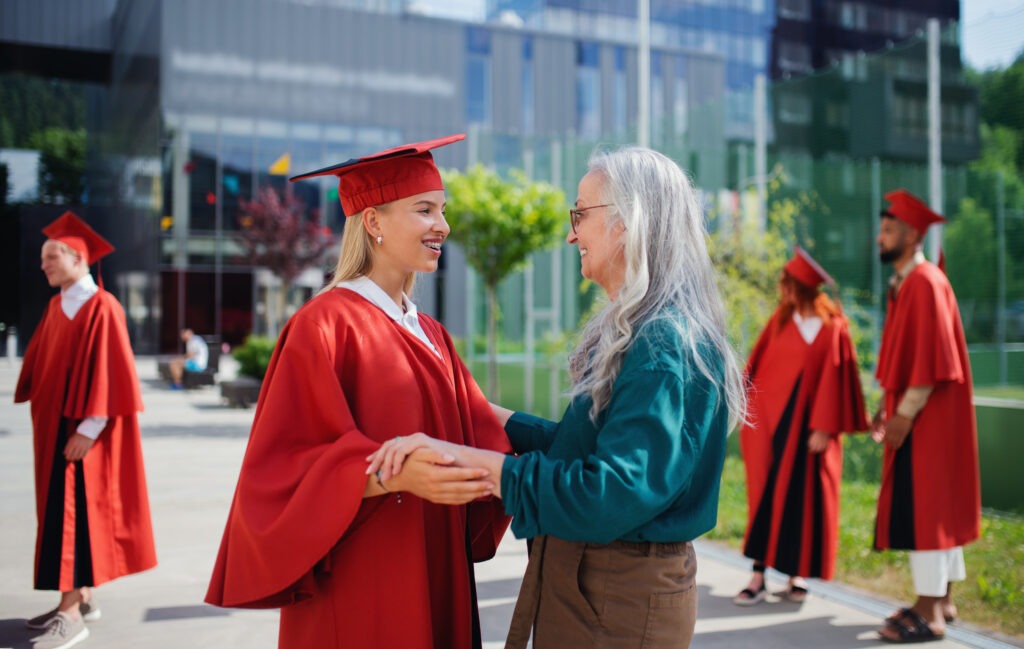 Portrait of cheerful university student with mother celebrating outdoors, graduation concept