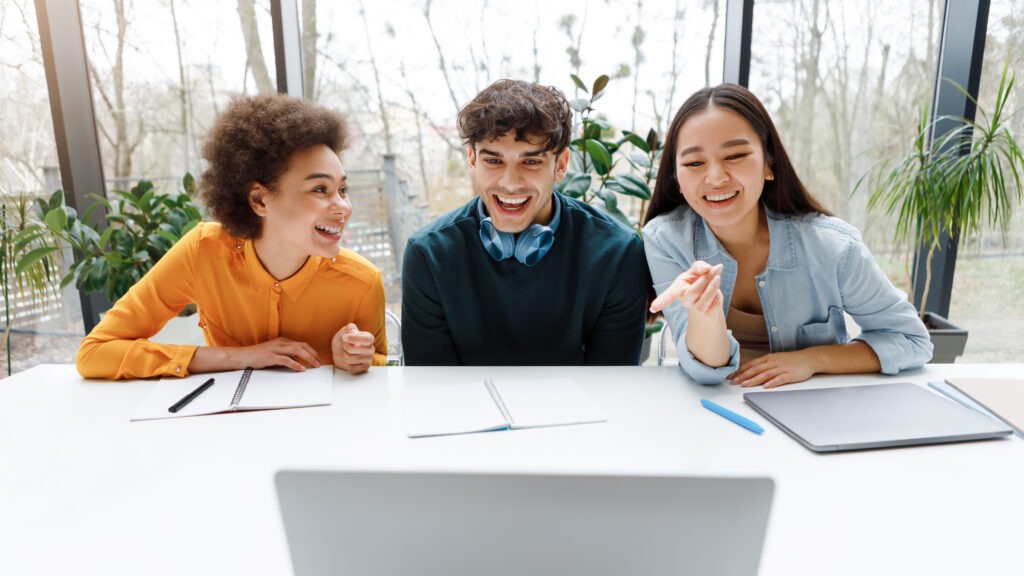 Group of international university students working with laptop, ladies pointing at screen and