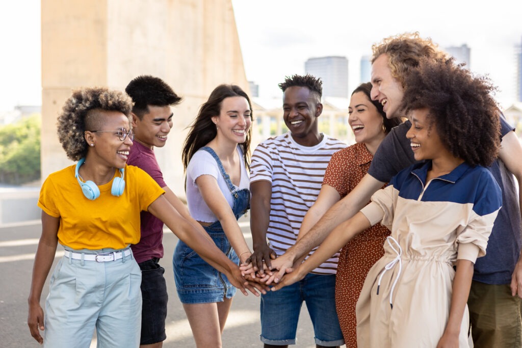 Group of young student friends with hands on stack showing international unity.