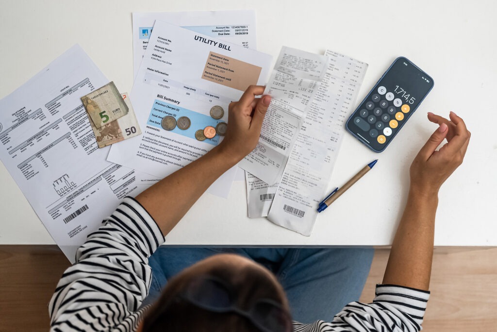 top view woman counts utility and bank bills sitting on floor, smartphone calculator and documents.