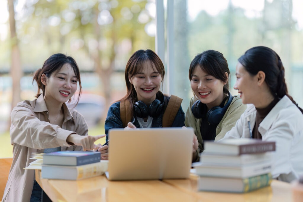 Group of young Asian college students sitting on a bench in a campus relaxation area, talking