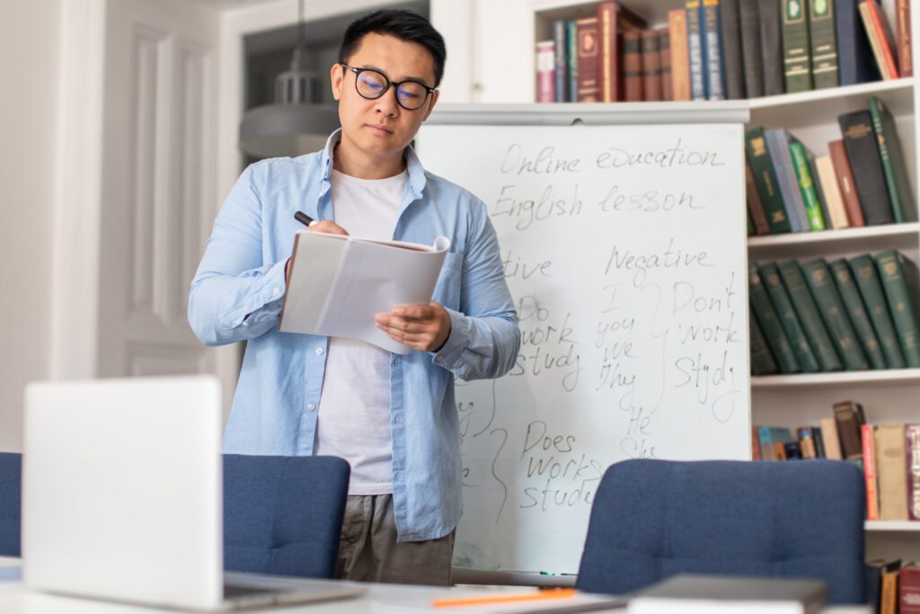 Japanese Male Teacher Taking Notes In Class Journal In Classroom