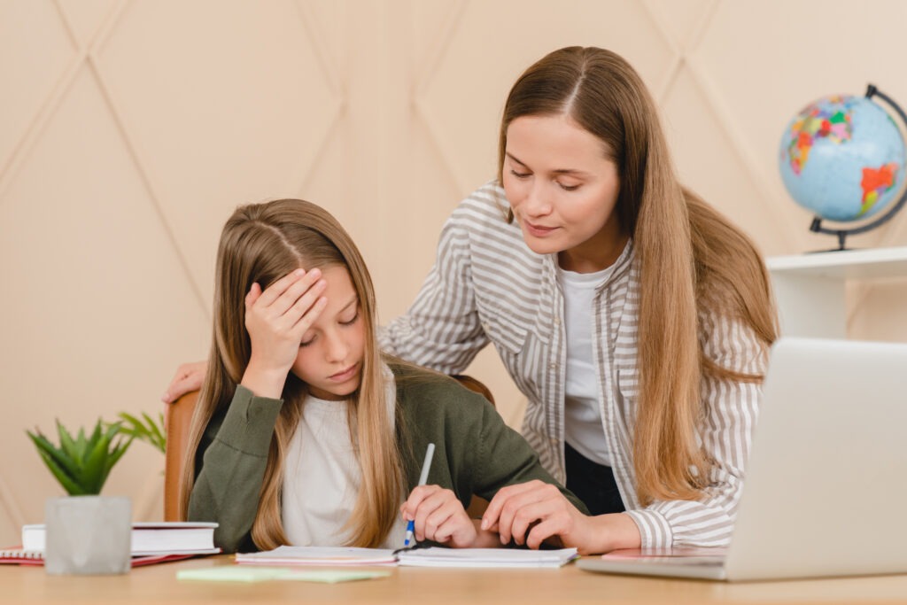 Overworked pupil doing difficult homework while tutor teacher mother helping with school preparation