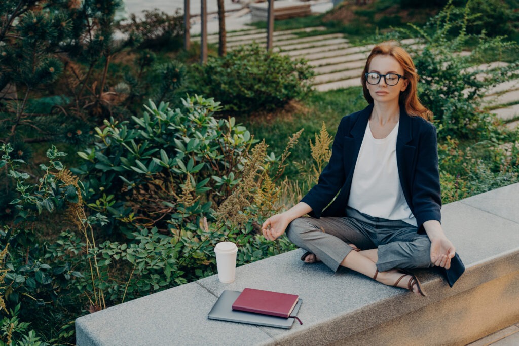 Peaceful calm redhead business woman doing yoga with closed eyes outdoor