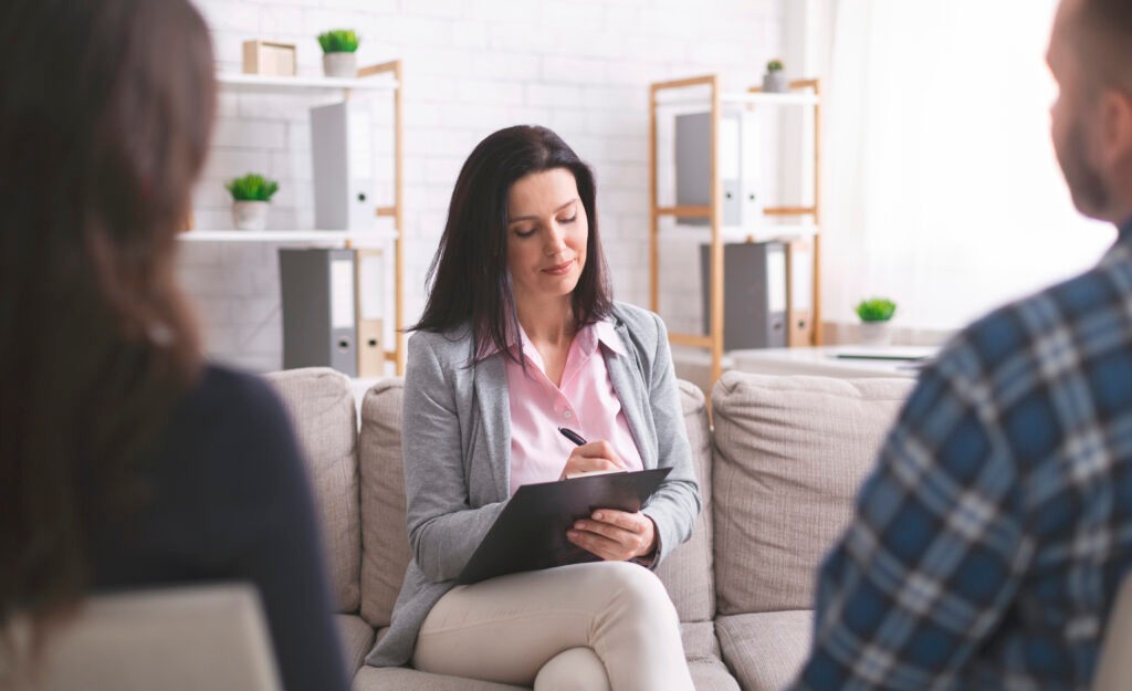 Professional psychologist taking notes at couple meeting with patients