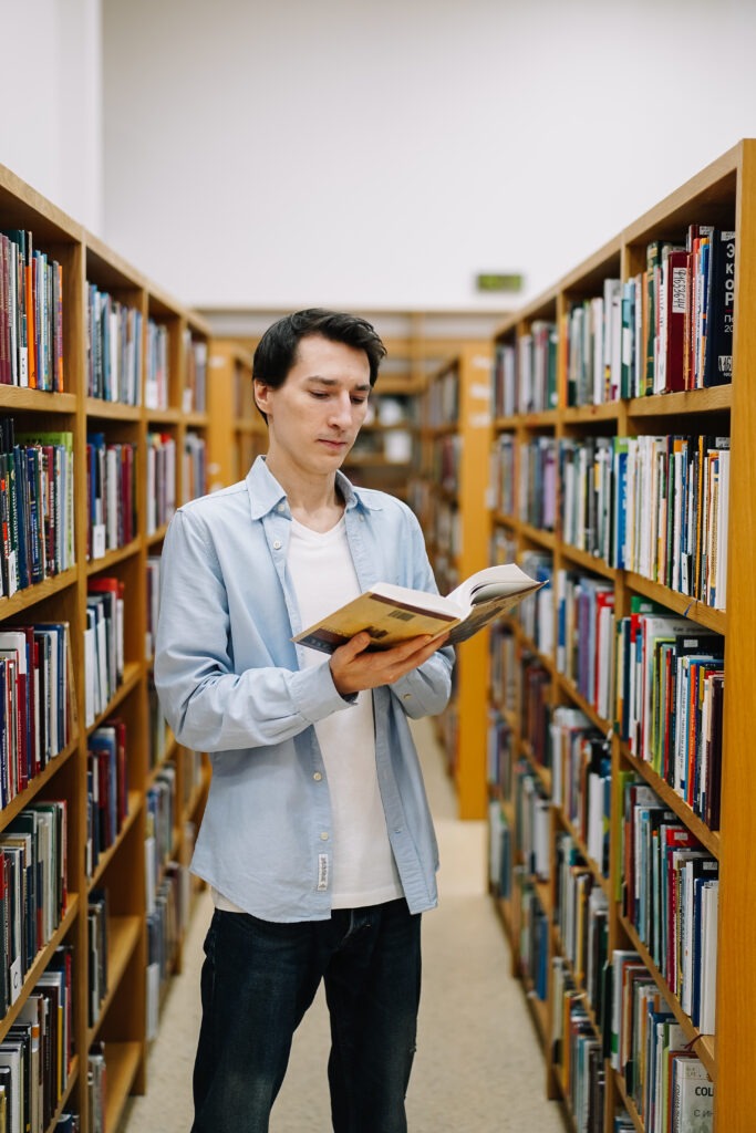 Young male student reading a book in a library. Portrait of male student holding book