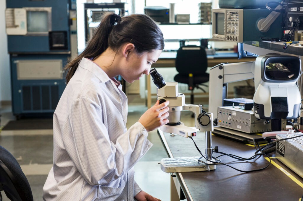 A caucasian female technician using a microscope in research and development