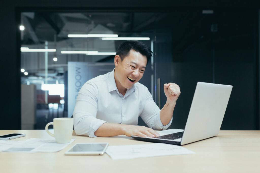 A young Asian man sits in the office looks at the laptop, participates in the auction, places bets