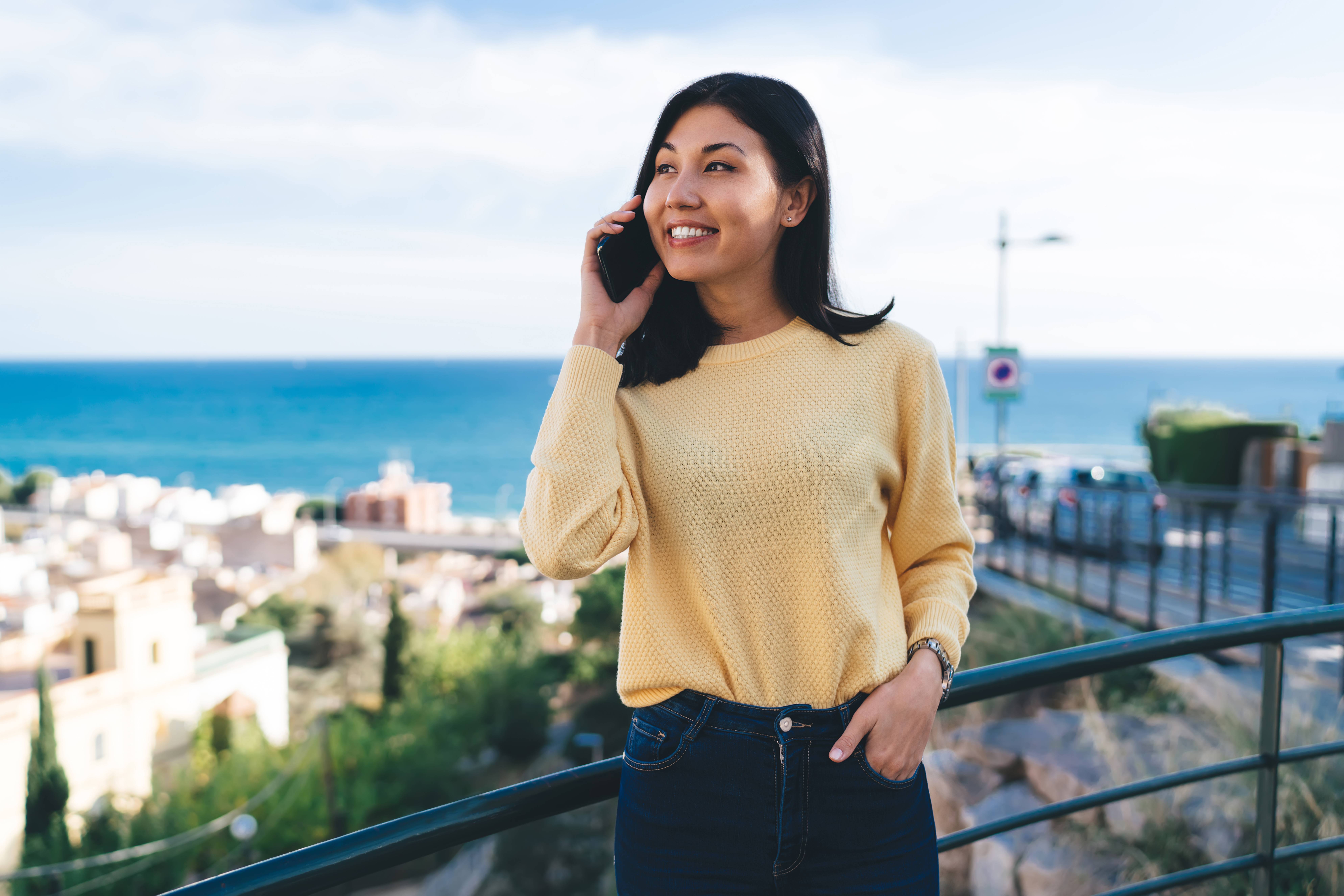 Happy Asian tourist laughing during international smartphone conversation