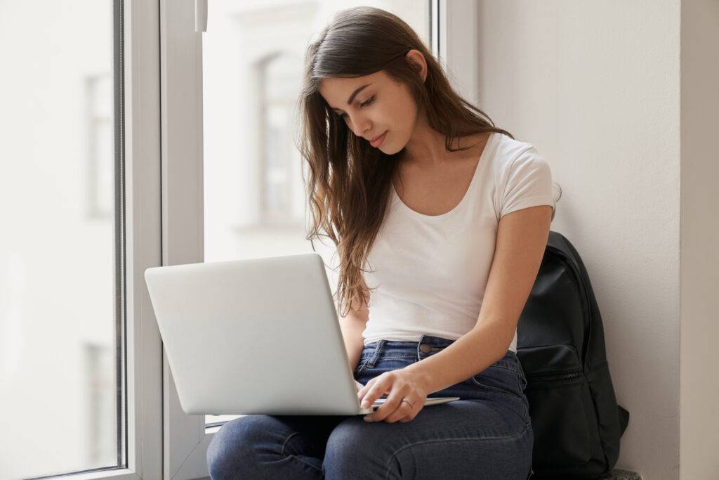 Pretty girl sitting on windowsill with laptop in university