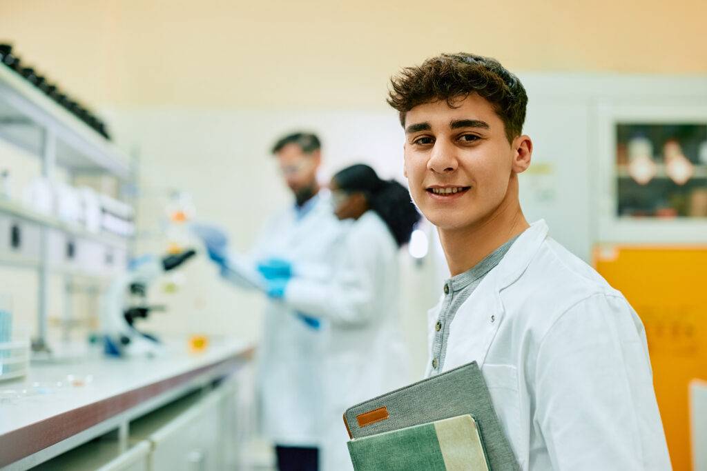 Young happy student of science in laboratory looking at camera.